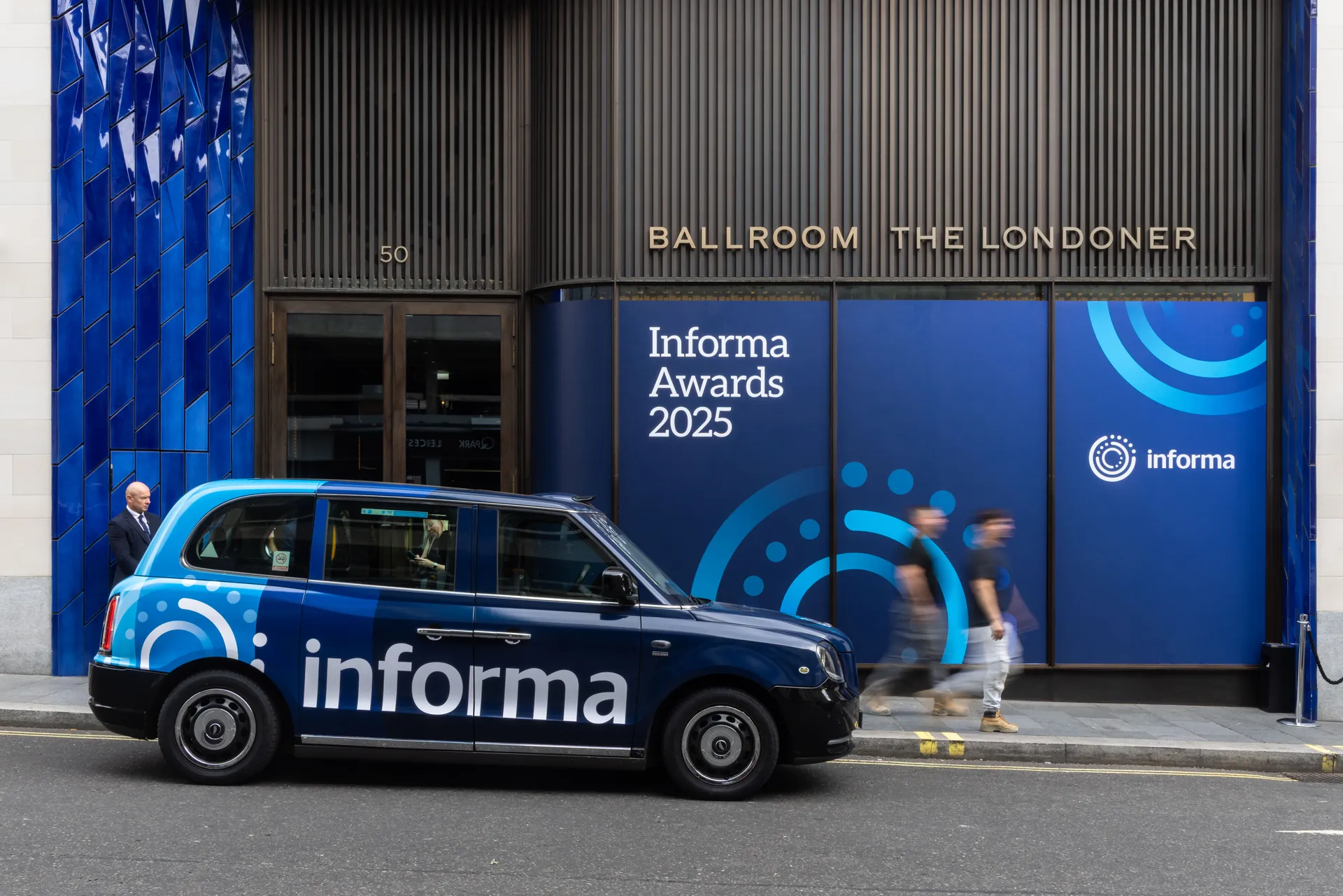 Blue Informa-branded taxi at the kerb outside The Londoner’s ballroom entrance