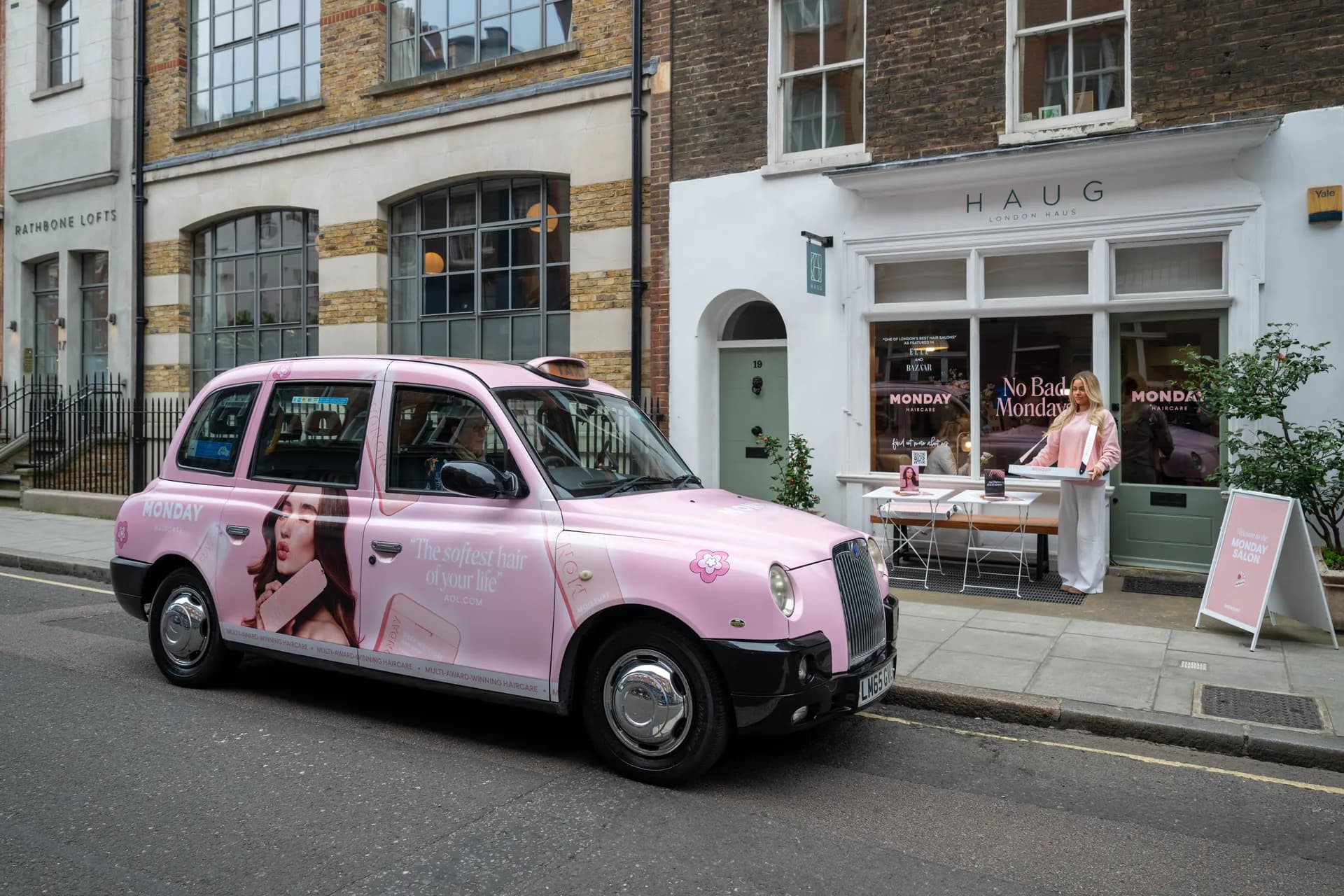 Pink Monday Haircare taxi parked outside a shop with a Monday display in the window