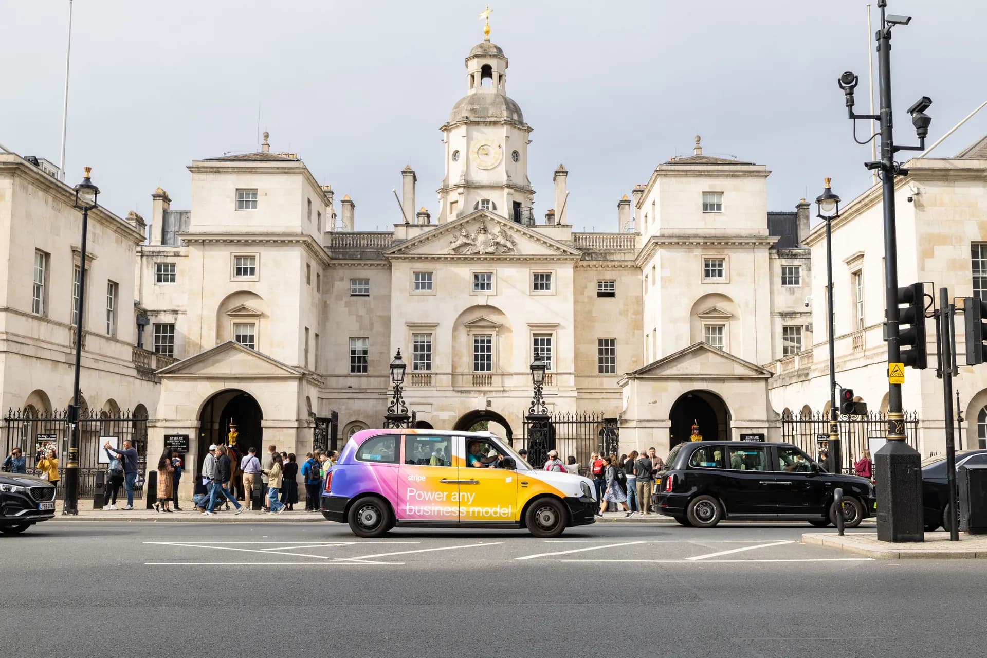 Taxi in pink, purple and yellow Stripe livery passing a historic building